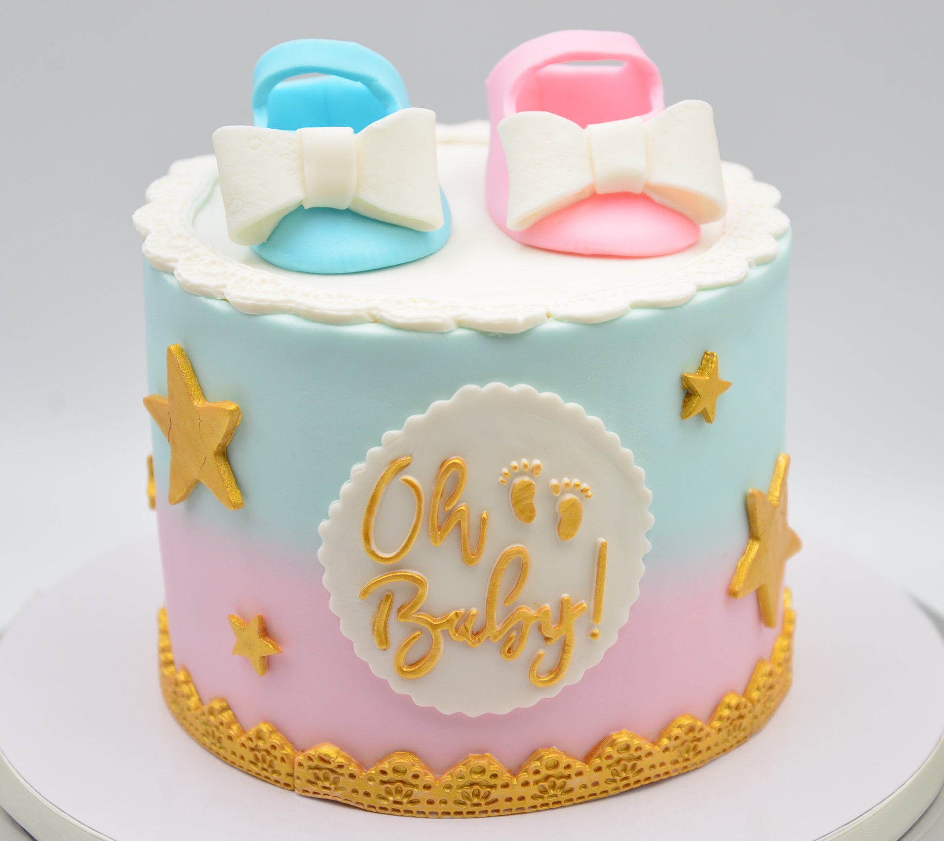 Blue and Pink ombre decorated gender reveal cake with stars, oh baby on the side and blue and pink shoes on top.